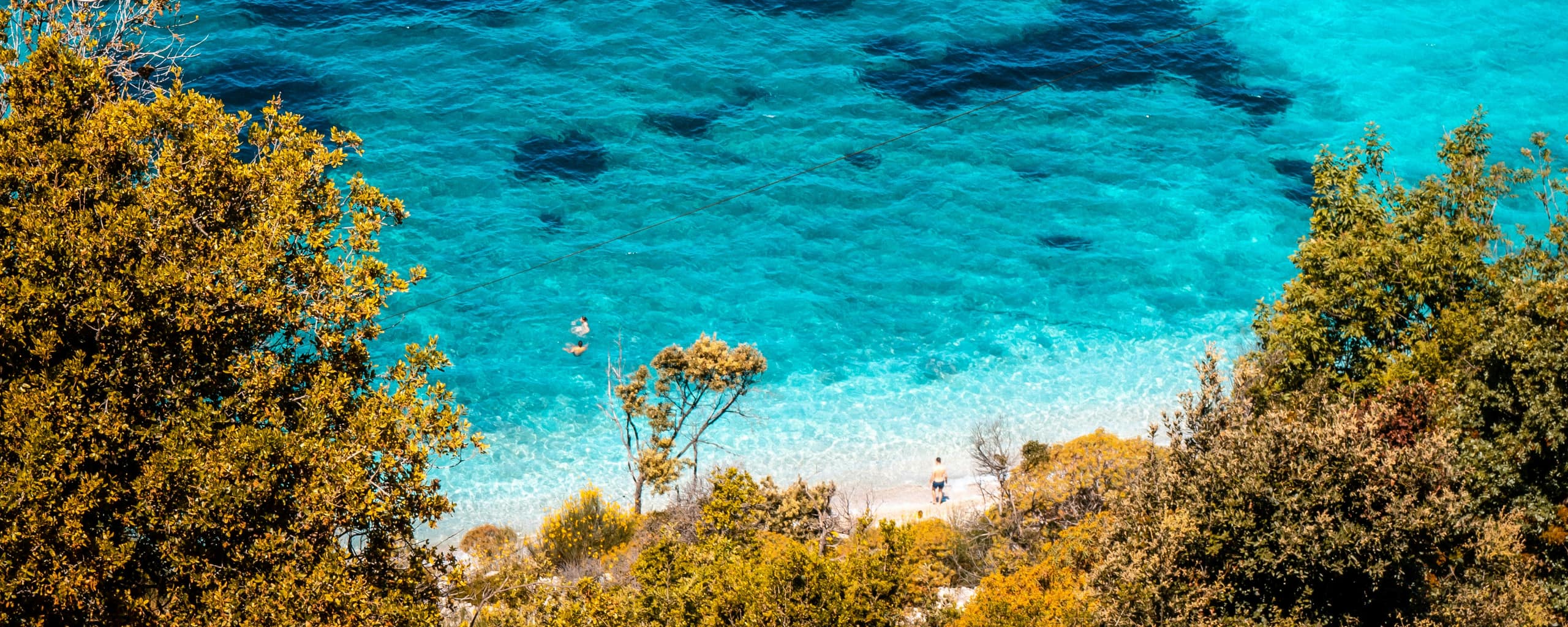 Klares Wasser der Bucht von Pulëbardha bei Ksamil, gerahmt von bewachsenen Hängen